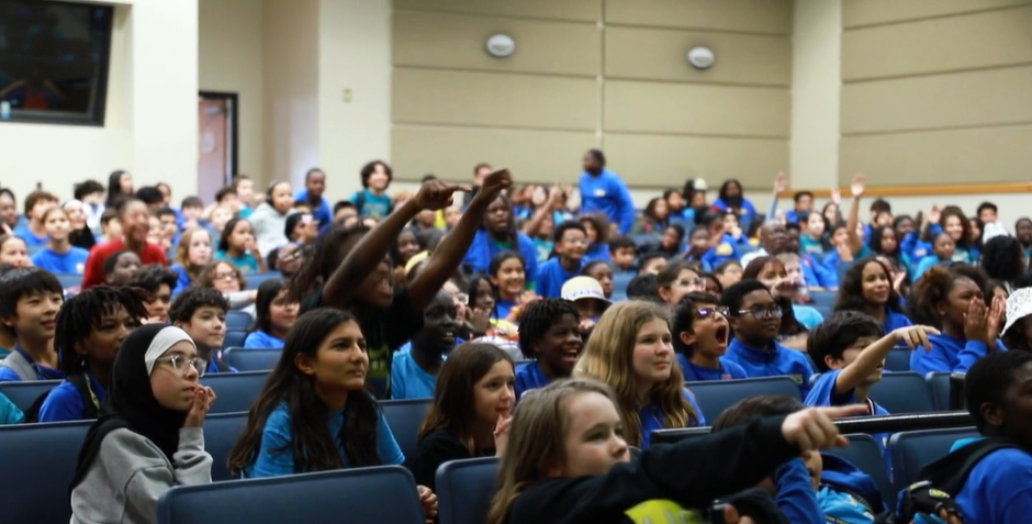 Middle school students cheering and raising their hands during a BrainAbouts assembly