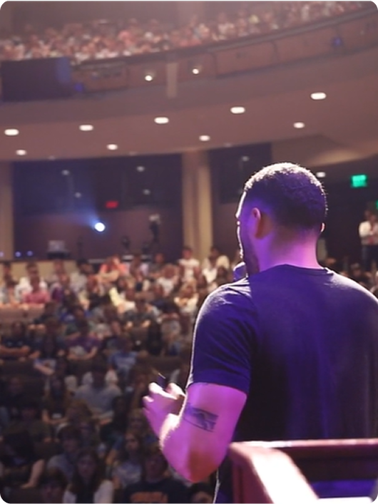 A presenter speaking to a full auditorium of high school students